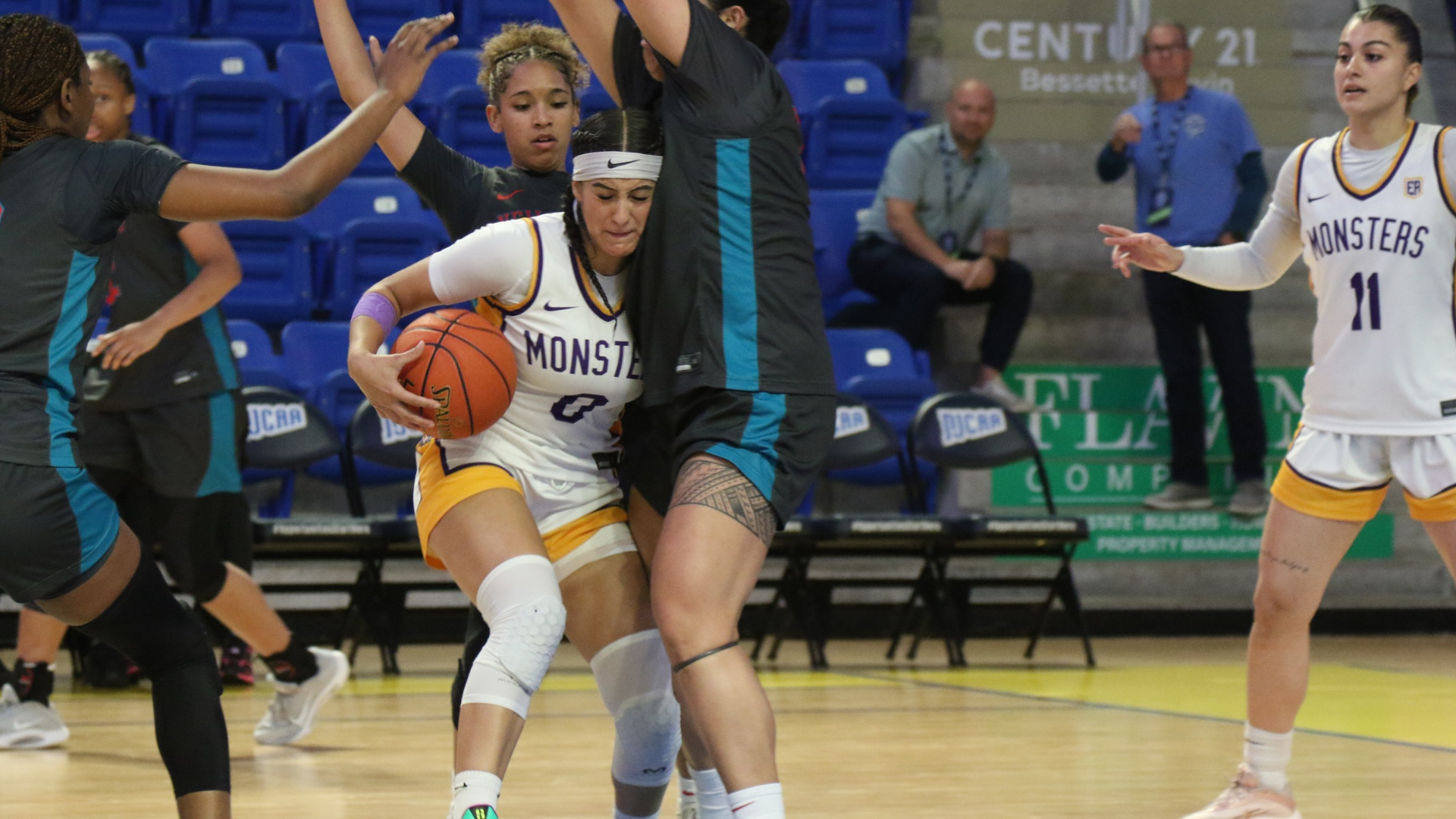 Eastern Arizona College Esmeralda Enriquez dribbles through defensive pressure during live game action, with teammates and opponents positioned around the lane inside an arena.